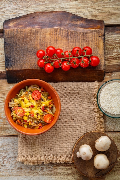 Risotto with mushrooms in a plate on a wooden background on a linen napkin next to tomatoes on a plank.