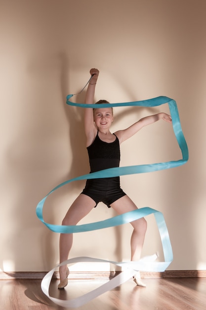 Ritmische gymnastiek. Sterke zelfverzekerde ballerina. Tienersport, gezonde tienerlevensstijl. Jong meisje met blauw lint in beweging, bruine achtergrond met vrije ruimte, ballet concept