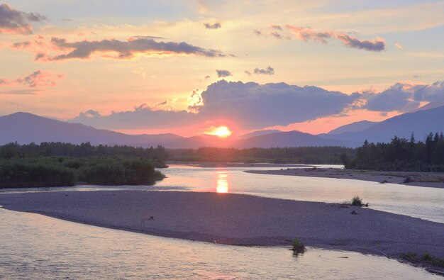 The river bank in the Altai mountains under the golden evening sky. Siberia, Russia