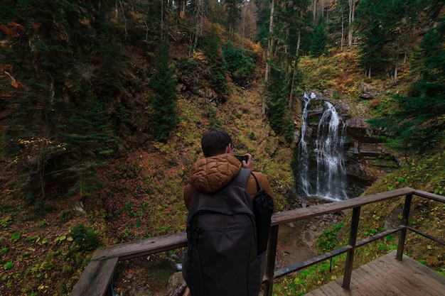 River deep in mountain forest. Nature composition. Mendelich River in the North Caucasus, Rosa Khutor, Russia, Sochi. Autumn forest, fog and rain. tourist takes a photo of a waterfall on a smartphone
