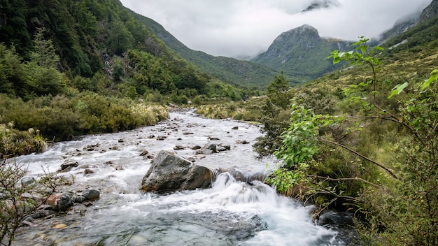 river flowing through the valley surrounded by mountains shrouded in cloudsnelson lakesnew zealand