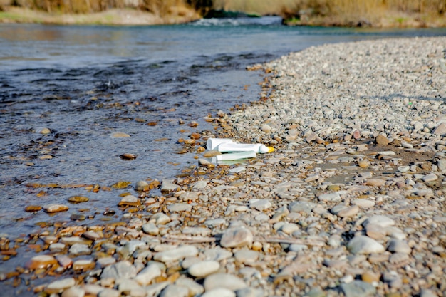 Загрязнение реки у берега, мусор у реки, пластиковые пищевые отходы, способствующие загрязнению.