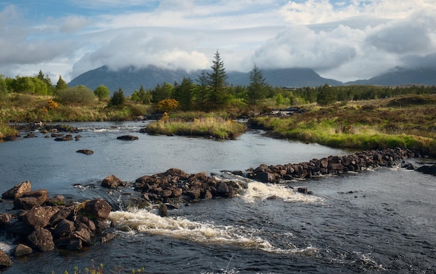 a river runs through a rocky landscape with a mountain in the background.