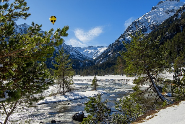 River in the snowy Pyrenees mountains with yellow hot air balloon