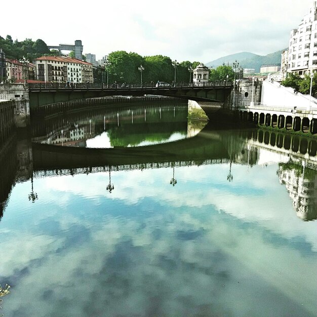 Foto rivier die de bewolkte lucht en de brug in de stad weerspiegelt