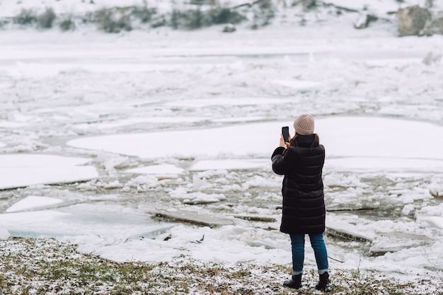 Rivier in de winter met een oppervlak bedekt met een dikke laag gebarsten ijs en ijsschotsen. meisje neemt foto.