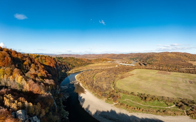 Rivierstroomversnellingen met herfstbossen op oevers onder blauwe lucht