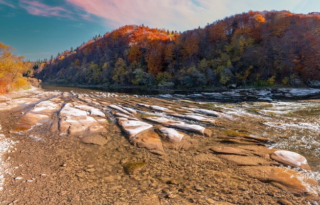 Rivierstroomversnellingen met herfstbossen op oevers onder blauwe lucht