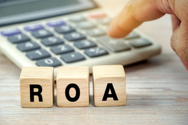 ROA - acronym from wooden blocks with letters. business concept finger background with blur calculat