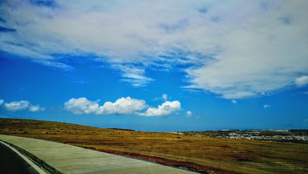 Road amidst field against blue sky