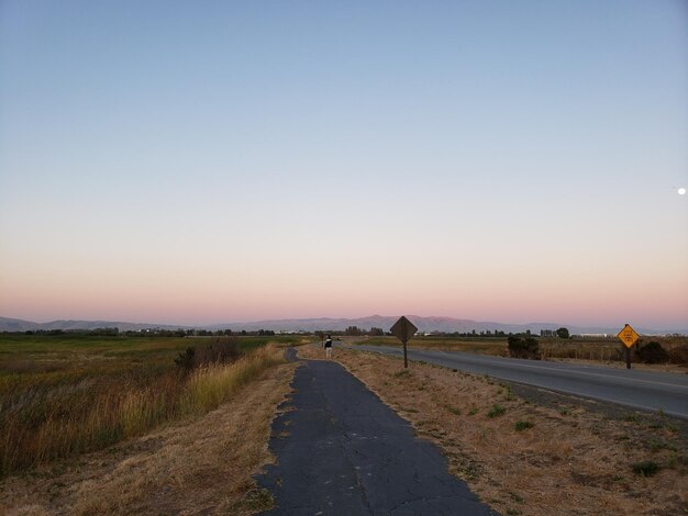 Road amidst field against clear sky during sunset