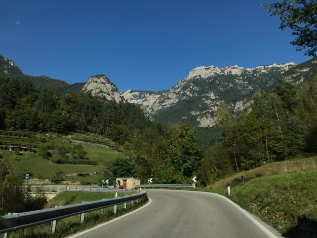 Road amidst trees and mountains against clear blue sky