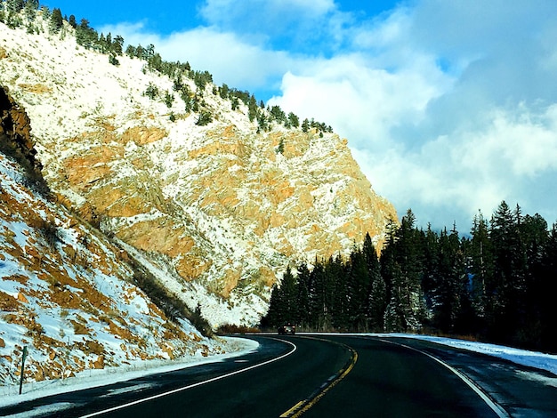 Photo road amidst trees and snowcapped mountains against sky