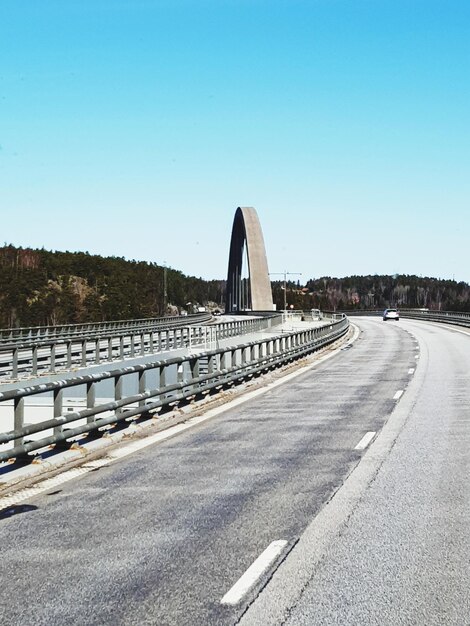 Road by bridge against clear blue sky in city