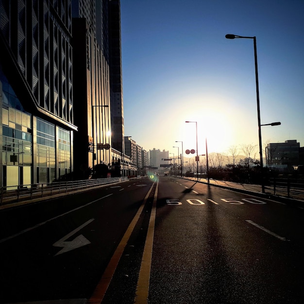 Road by buildings against sky during sunset in city