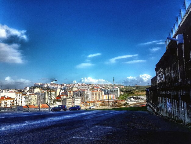 Road by cityscape against blue sky