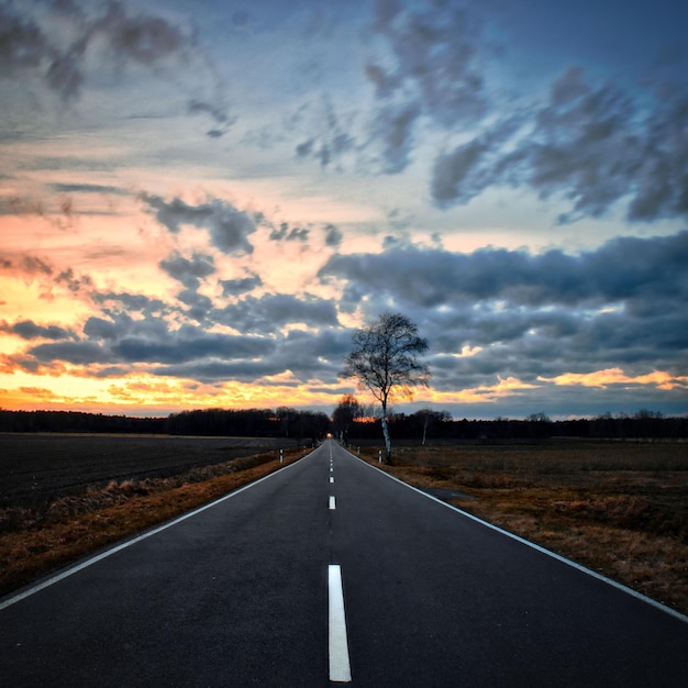 Road by landscape against sky during sunset