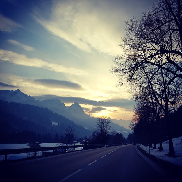 Road by silhouette mountains against sky at sunset