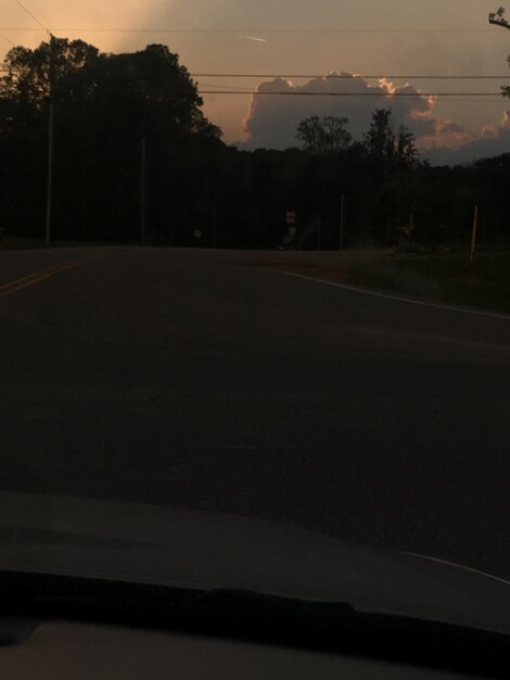 Road by silhouette trees against sky at sunset