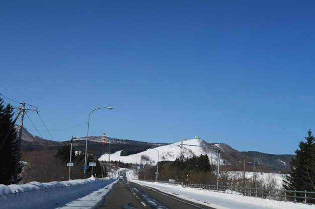 Road by snowcapped mountains against clear blue sky