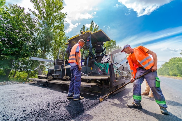 Road construction with working commercial equipment heavy\
machinery on road repair workers on construction site