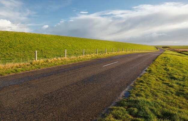 Дорога между зелеными травяными холмами под голубым небом