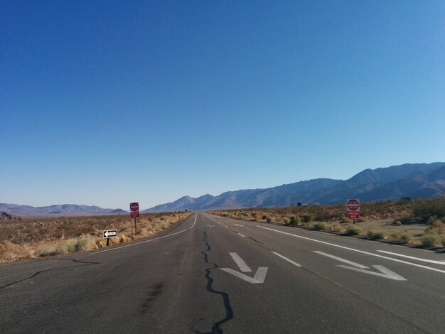 Road leading to mountains against clear blue sky