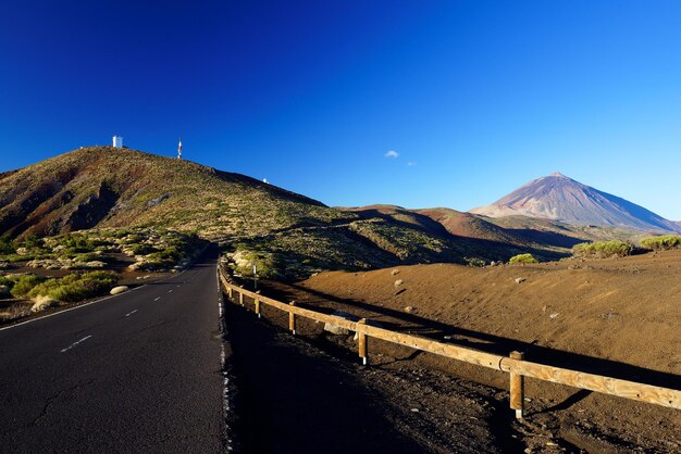 Foto la strada che porta verso la montagna verde contro un cielo blu limpido