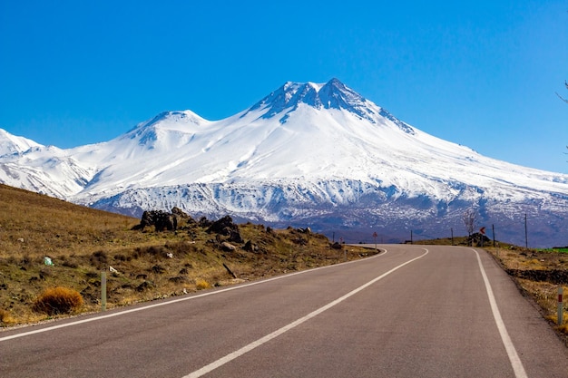 Foto la strada che porta verso la montagna innevata contro il cielo blu