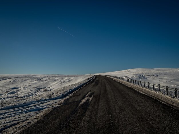 Road leading towards snowcapped mountains against clear blue sky