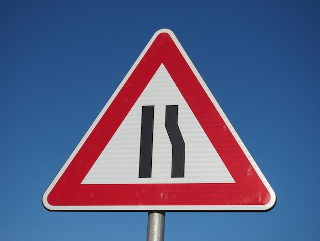 Road narrows sign over blue sky