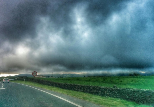 Photo road passing through field against cloudy sky