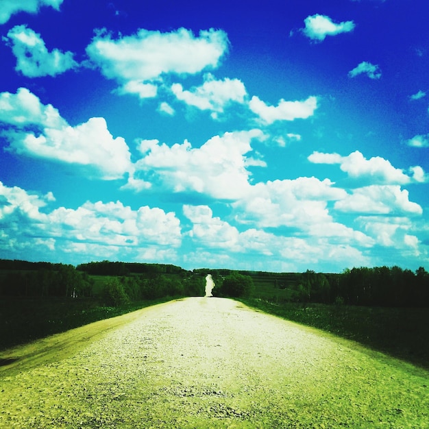 Foto strada che attraversa un campo contro un cielo nuvoloso