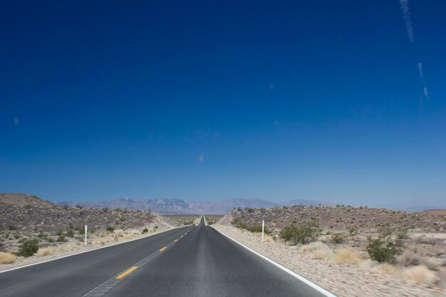 Road passing through landscape against clear blue sky