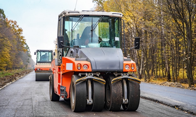 道路の修理、コンパクターはアスファルトを敷きます。重い特殊機械。稼働中のアスファルトペーバー。側面図。閉じる。