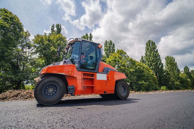 道路の修理、コンパクターはアスファルトを敷きます。重い特殊機械。稼働中のアスファルトペーバー。側面図。閉じる。