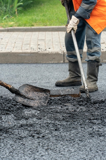 市内の道路修理 道路の穴やくぼみを新しいアスファルトで埋めている ブーツとオーバーオールを身に着け、さまざまな装備を手にしたビルダーが新しいアスファルトを敷設しています