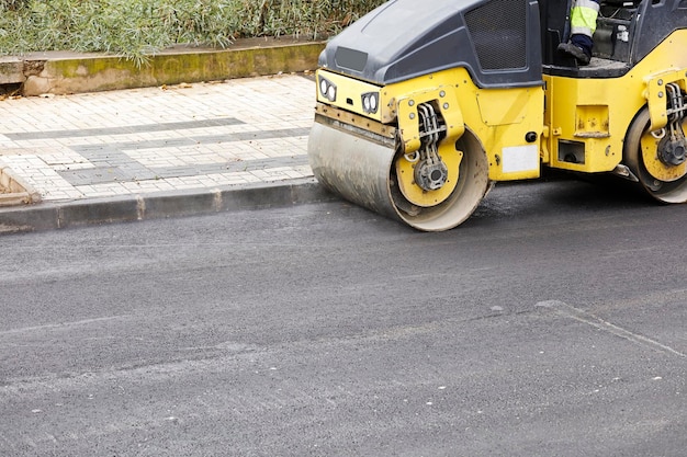 Road roller and asphalt paver machine at the construction site, with hot concrete and smoke