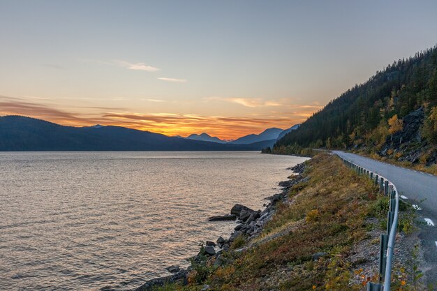 The road running along the lake at sunset goes into the mountains.