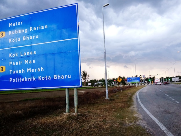 Road sign by street against cloudy sky