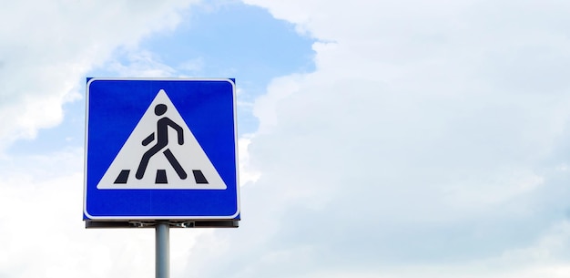 Road sign crossing for a pedestrian on a sky background with clouds