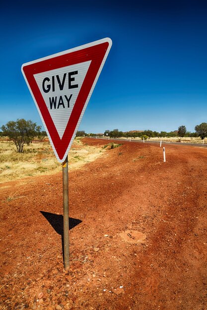 Road sign on field against clear blue sky