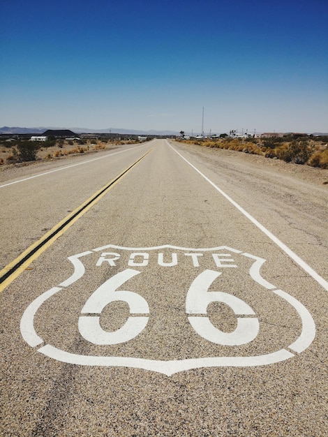 Road sign on landscape against clear blue sky