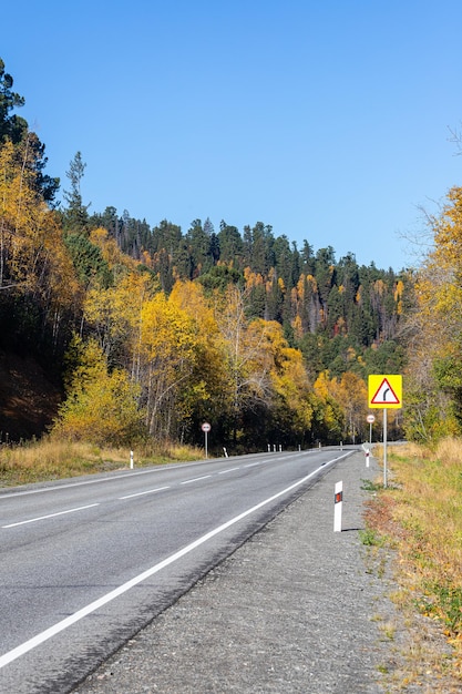 Strada principale del segnale stradale sullo sfondo della foresta autunnale e del cielo blu