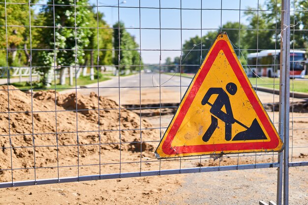 Road sign Roadworks ahead on the fence against the background of a trench across an empty street