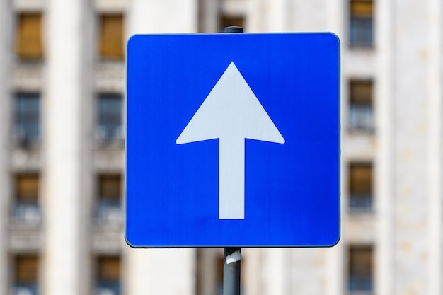 Photo road sign for single circulation direction white arrow on blue panel towards clear blue sky