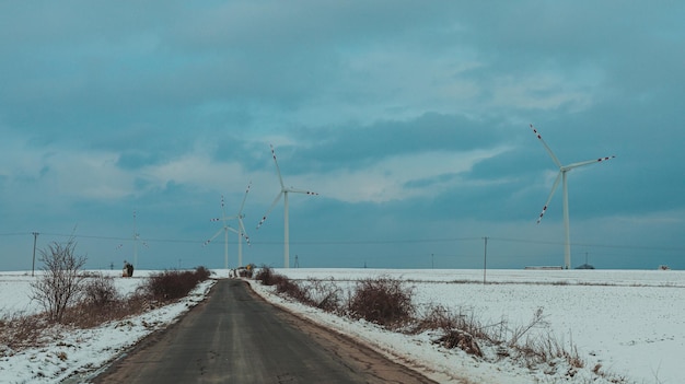 Road between snowy fields with windmills in the background