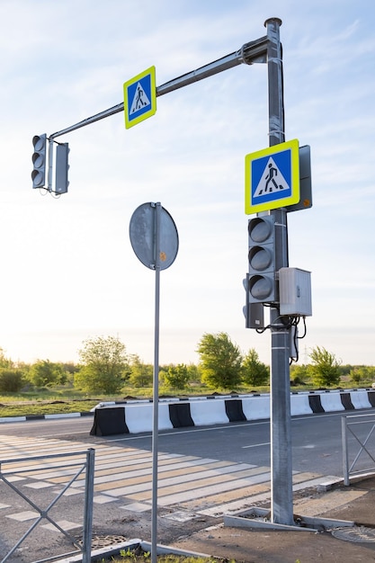 On the road there is a pole with two traffic lights and two traffic signs The traffic lights don't work Road signs Crosswalk