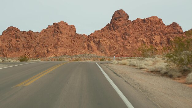 미국 네바다주 라스베이거스 밸리 오브 파이어에서 자동차를 운전하는 로드 트립. 미국을 여행하는 히치하이킹, 고속도로 여행. 붉은 외계 암석, 모하비 사막 황야는 화성처럼 보입니다. 차에서 봅니다.