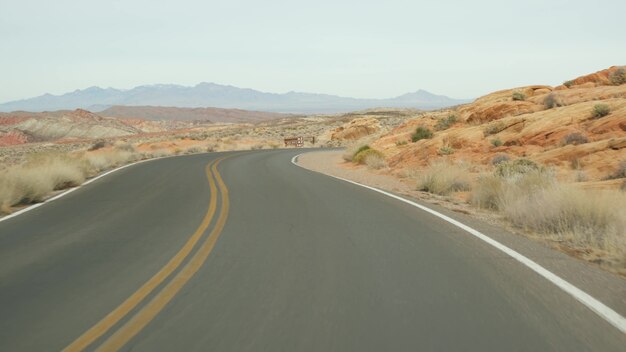 Road trip, driving auto in Valley of Fire, Las Vegas, Nevada, USA. Hitchhiking traveling in America, highway journey. Red alien rock formation, Mojave desert wilderness looks like Mars. View from car.